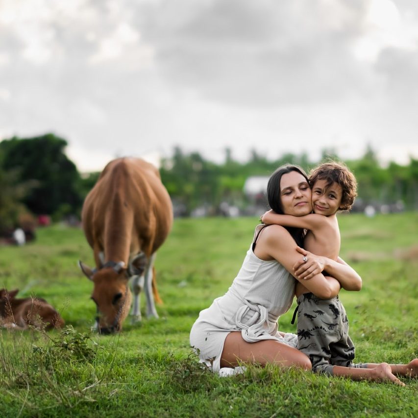 Madre e hijo abrazados en el prado entre las vacas