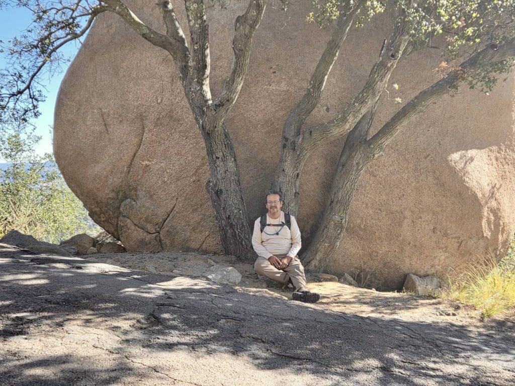 Person sitting in meditation beneath a large boulder and tree