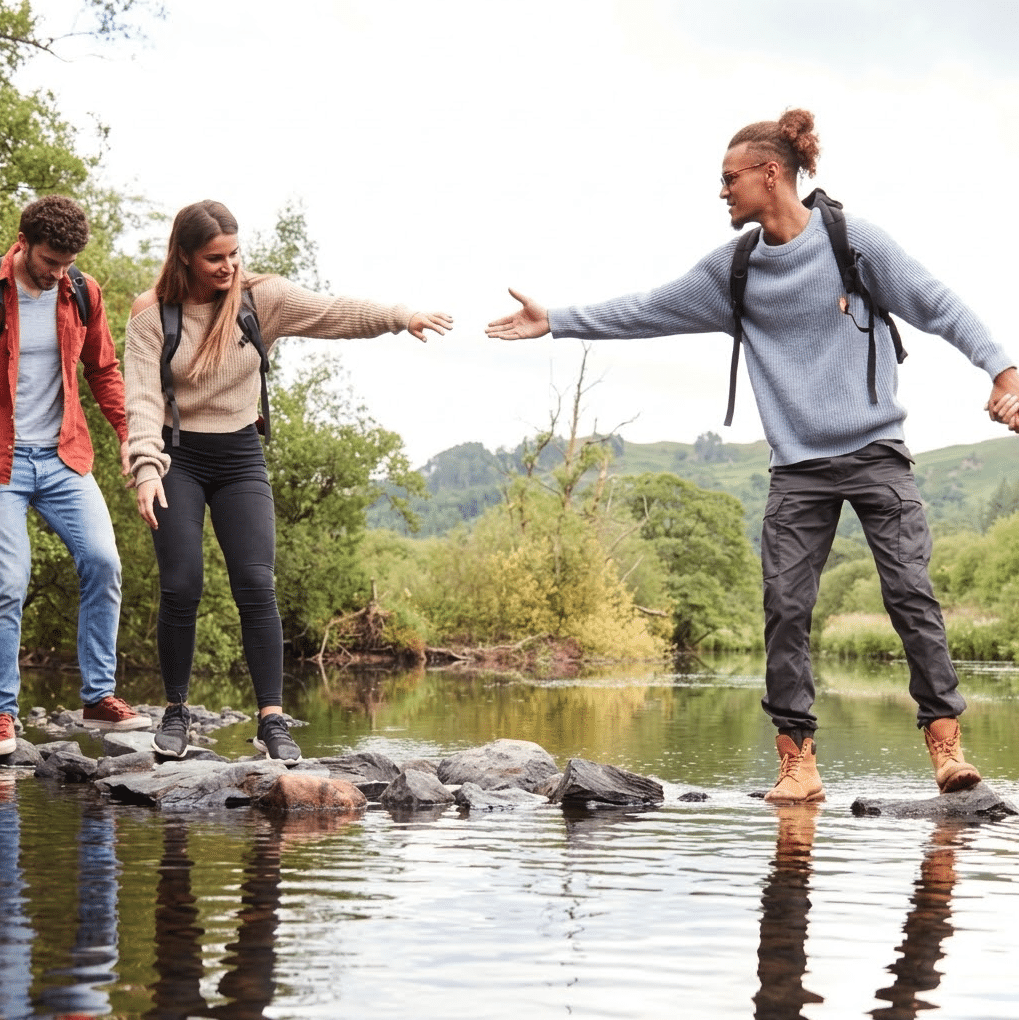Friends helping each other cross a river on stepping stones