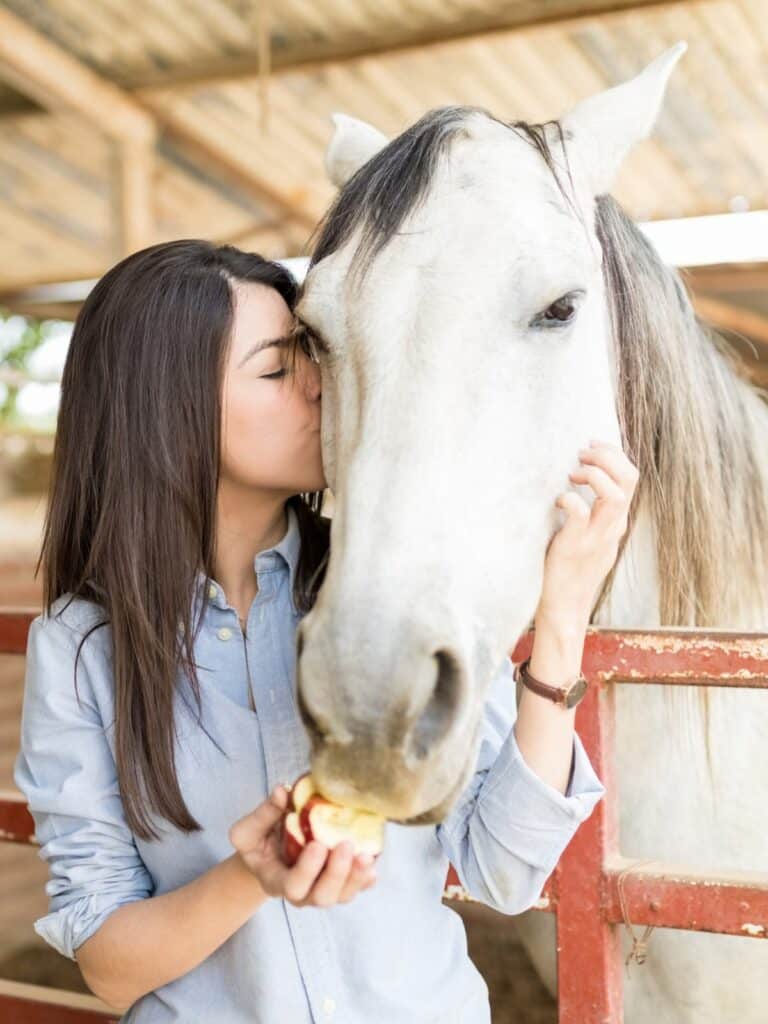 Woman resting her face against a white horse