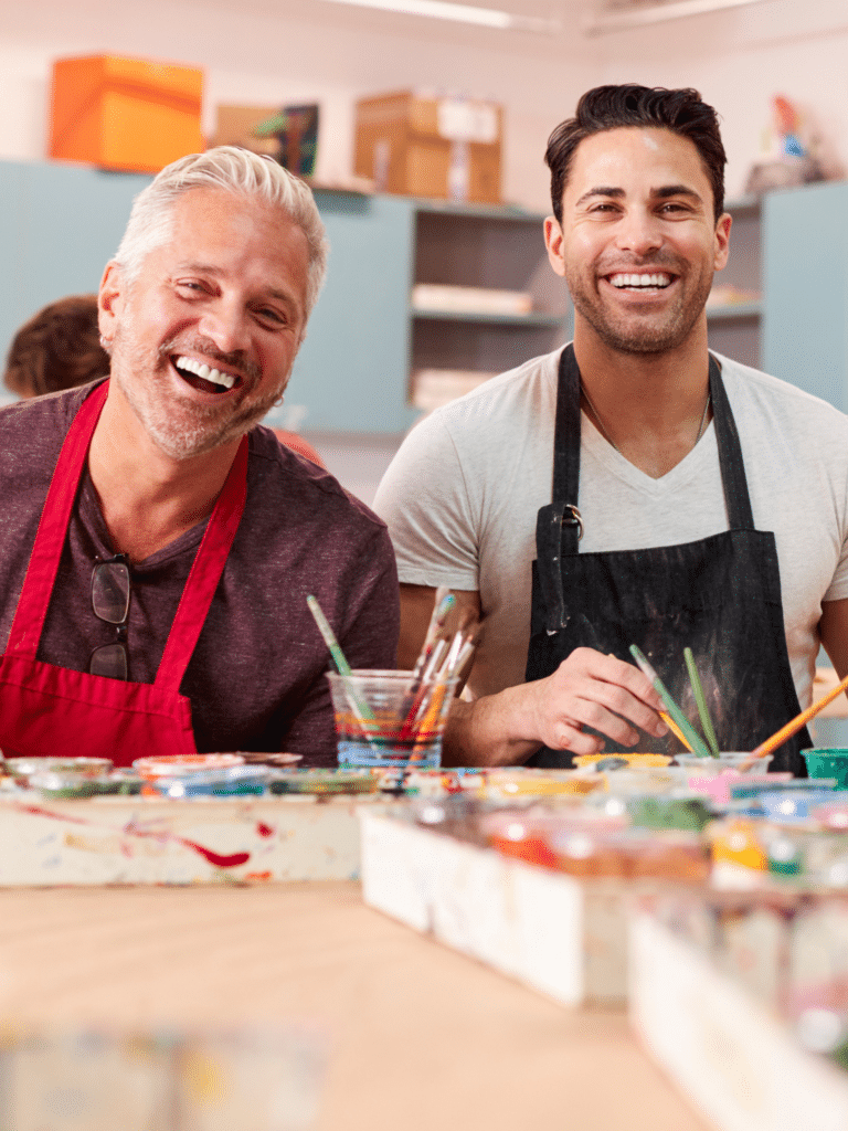 Two smiling men painting together in an art therapy class