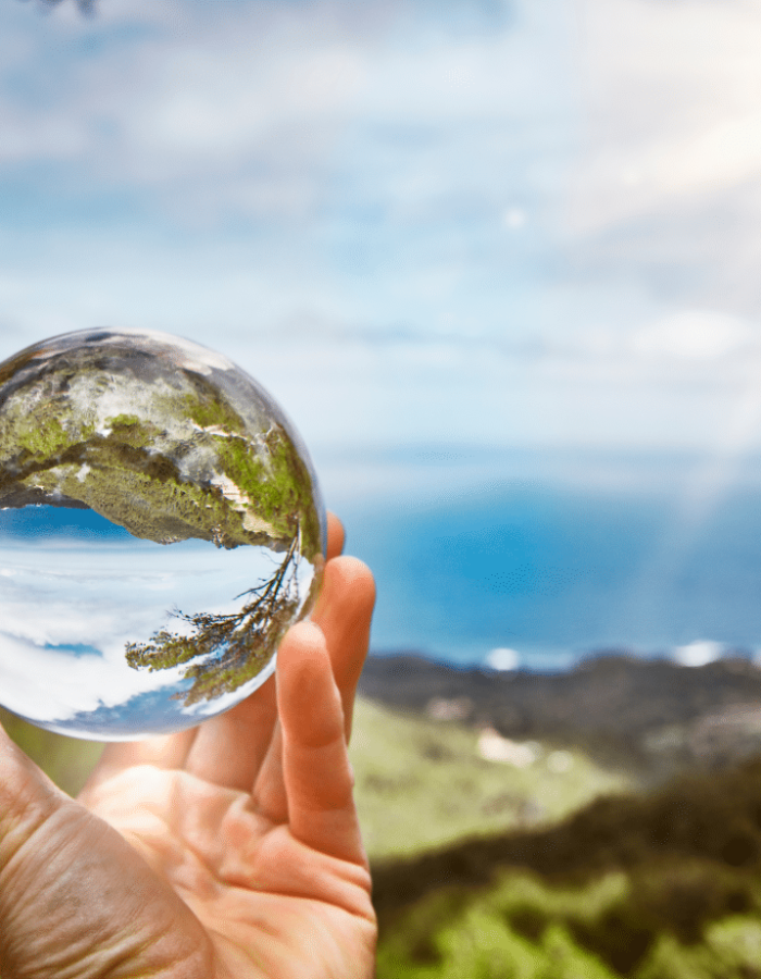 Hand holding a glass sphere reflecting the ocean and hills